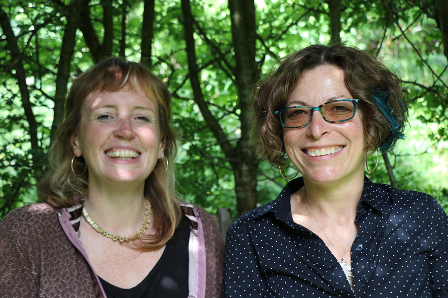 Bethan Prosser & Bela Emerson (photo by Sarah West): close up of two smiling women sitting infront of trees